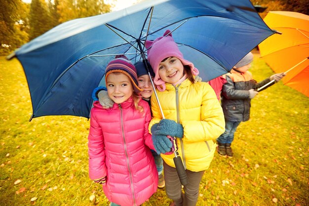 childhood, friendship, season, weather and people concept - group of happy kids with umbrella in autumn park