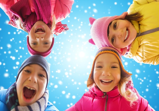 childhood, friendship, winter, christmas and people concept - happy little children faces outdoors over blue sky and snow background