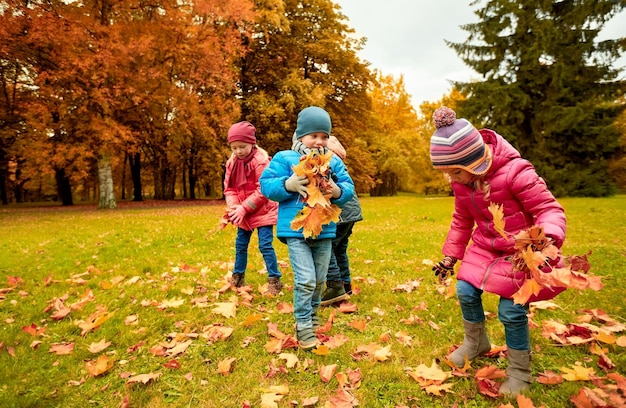 childhood, leisure, autumn, friendship and people concept - group of children collecting leaves in park