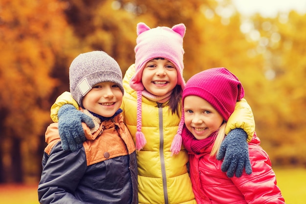 childhood, leisure, friendship and people concept - group of happy kids hugging in autumn park