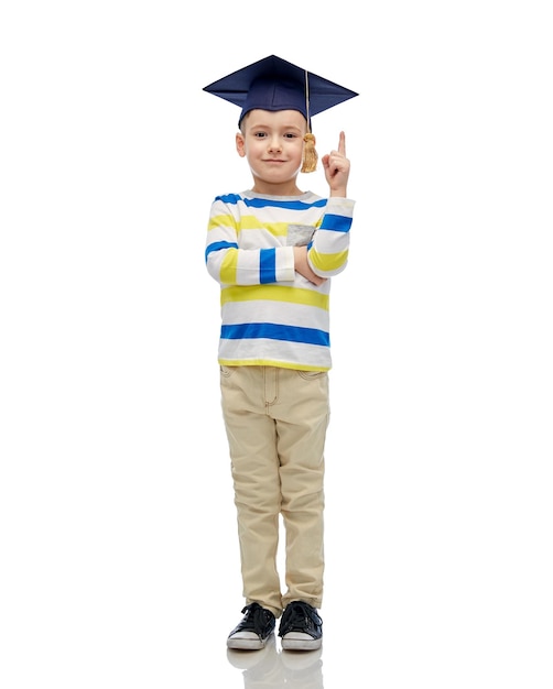 childhood, school, education, learning and people concept - happy boy in bachelor hat or mortarboard pointing finger up