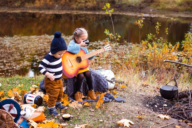 children in the autumn forest on a picnic grill sausages and play the guitar