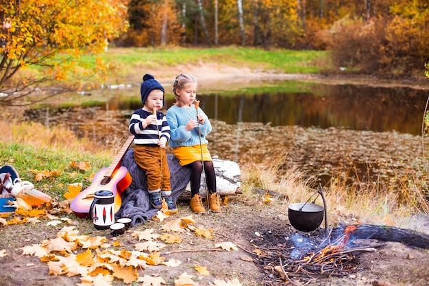 children in the autumn forest on a picnic grill sausages and play the guitar