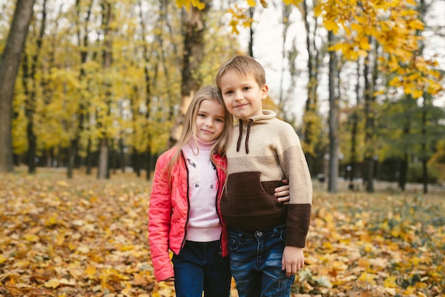 Children a boy and a girl have fun and hug in the autumn forest among the fallen leaves