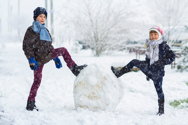 Children boy and girl outdoors in snowy winter are making a big snowman