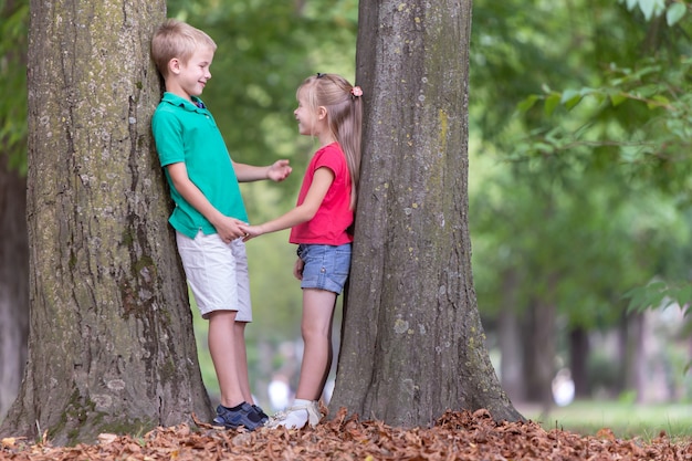 Children boy and girl standing near big tree trunk in summer park