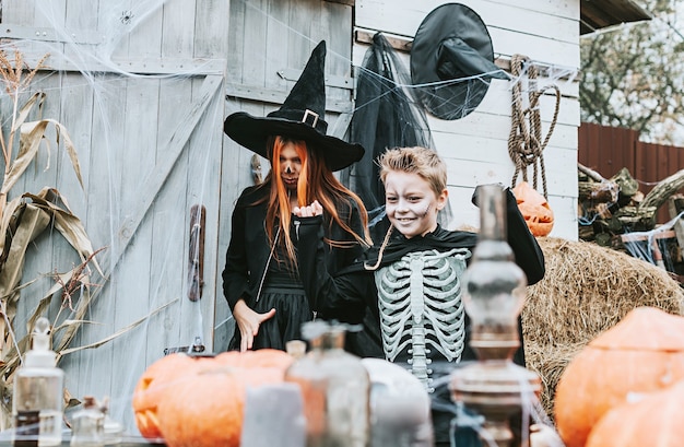 Photo children a boy in a skeleton costume and a girl in a witch costume having fun at a halloween party on the decorated porch