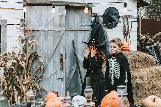 Photo children a boy in a skeleton costume and a girl in a witch costume having fun at a halloween party on the decorated porch