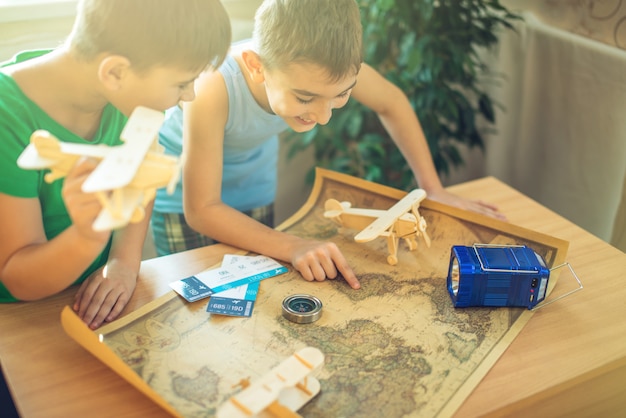 Photo children boys with airplane in hand, explore the map below to travel to new adventures.