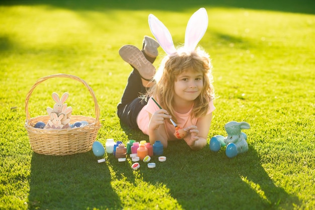 Children celebrating easter kid in rabbit costume with bunny ears painting eggs outdoor