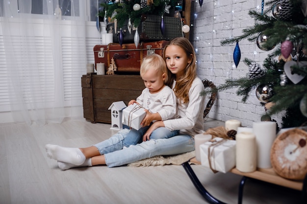 Children under Christmas tree with gift boxes. New Year's decorations. rustic style, dark wood decorations New Year's interior. Sisters.