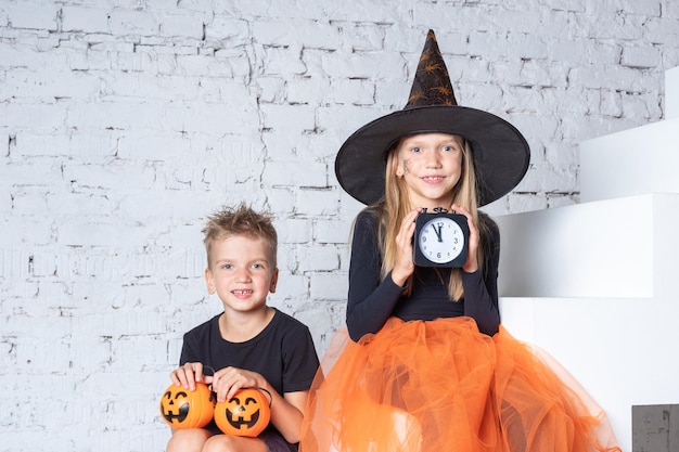 Children in creepy witch costumes and hats are holding a black alarm clock and a pumpkinshaped basket