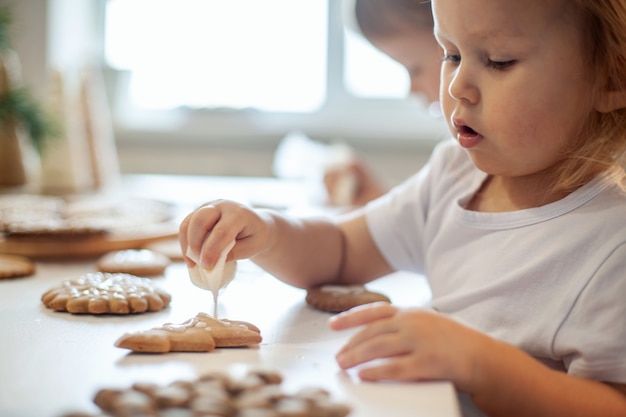 Children decorate christmas gingerbread at home a boy and a girl paint with cornets with sugar icing...