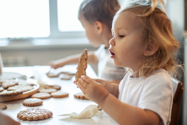 Children decorate christmas gingerbread at home a boy and a girl paint with cornets with sugar icing...