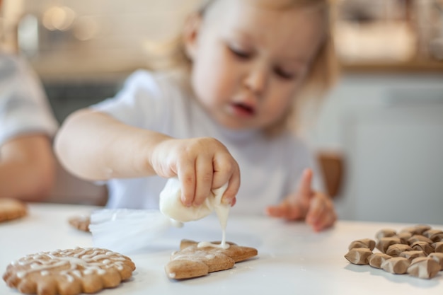 Children decorate christmas gingerbread at home a boy and a girl paint with cornets with sugar icing...