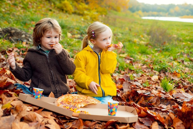 Children eating pizza on autumn fall time in nature