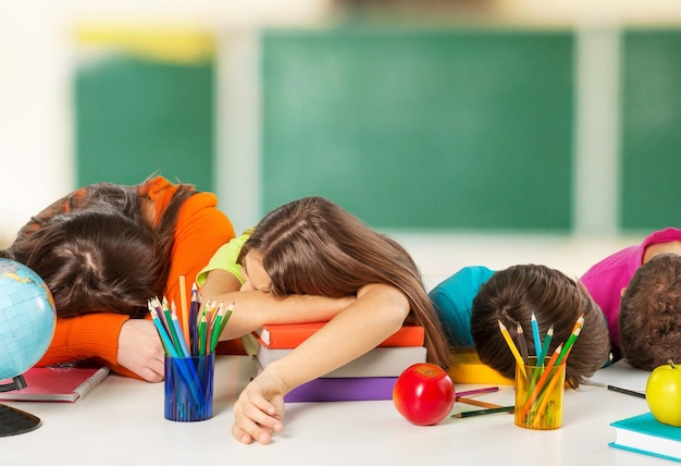 Children fall asleep on table while doing homework on classroom background