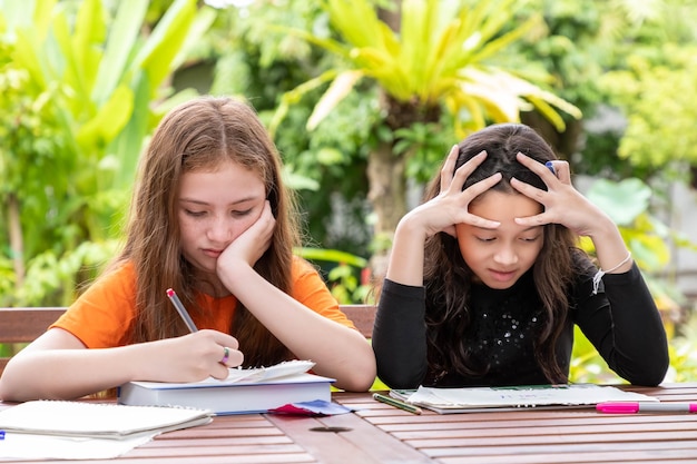 Children girls doing homework and drawing together in garden at home thinking seriously for solution