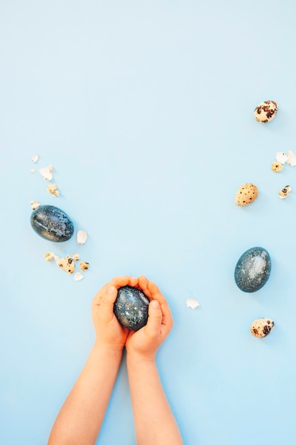 Children hands holding Easter blue color eggs close to eggshell on the light blue background Top view Easter concept Vertical orientation