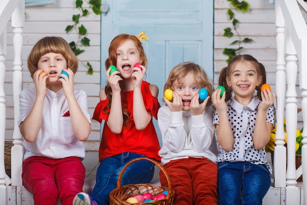 Children holding easter eggs. Beautiful children sit near the basket with tulips and hold Easter eggs in their hands. Funny moments