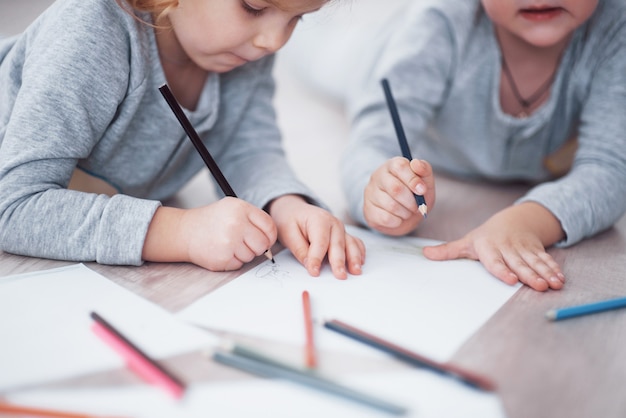 Children lie on the floor in pajamas and draw with pencils. Cute child painting by pencils. Hand of child girl and boy draw and paint with crayon. Close up view.