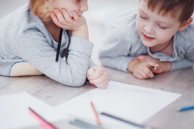 Children lie on the floor in pajamas and draw with pencils. Cute child painting by pencils.Hand of child girl and boy draw and paint with crayon. Close up view