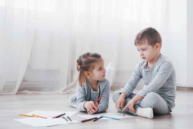 Children lie on the floor in pajamas and draw with pencils. Cute child painting by pencils