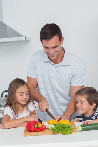 Children looking at their father who is cutting vegetables