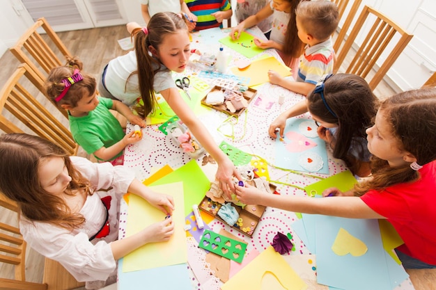 Children make handycrafts, little boys and girls sit around the table and make handmade postcards together