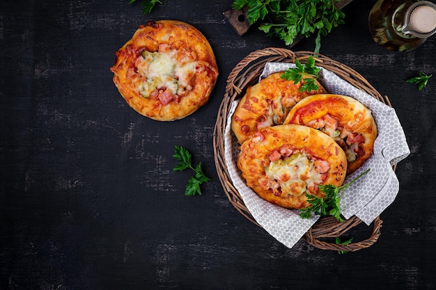 Children mini pizza small open pies with ham tomato sauce mozzarella and cheese in basket on a dark background Top view