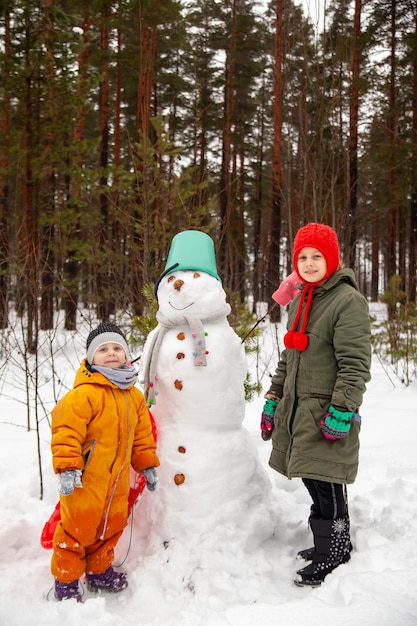 Children of nine and three years old on winter walk near snowman