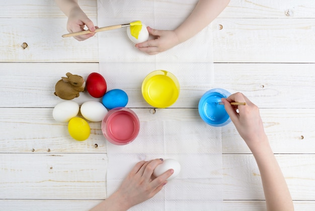 Children paint eggs for Easter on the wooden table