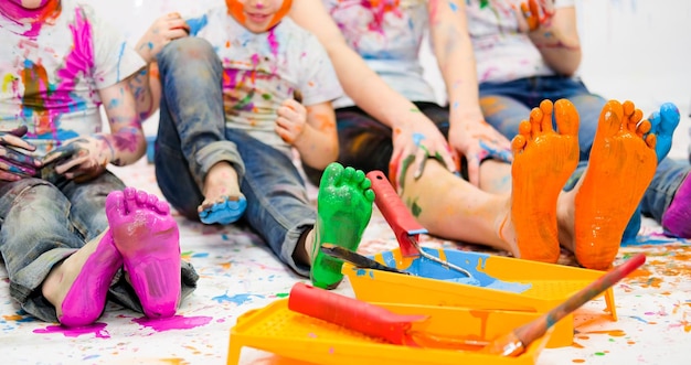 Children paint together with bright colors and their feet and faces are stained with paint