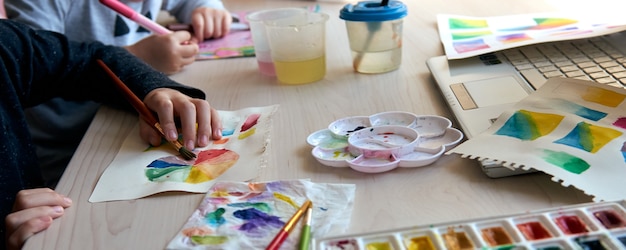 Children painting pictures with watercolor paints during art lesson. Pupils are concentrating on drawing with brush. Watercolor color wheel and palette. Color theory beginner hobby lessons