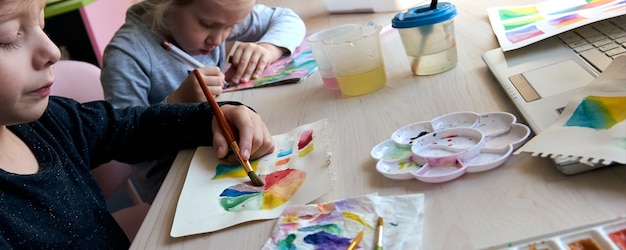 Children painting pictures with watercolor paints during art lesson. Pupils are concentrating on drawing with brush. Watercolor color wheel and palette. Color theory beginner hobby lessons.