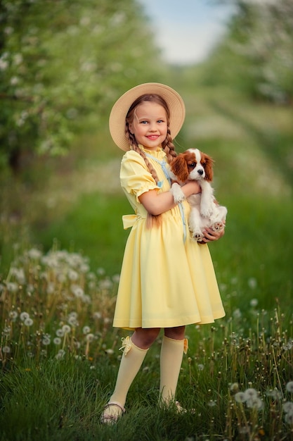 Children and pets cute little girl in a hat with pigtails holding a brown puppy cavalier king charles spaniel in her arms