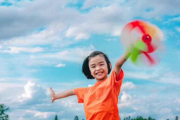 Children playing rainbow pinwheel or windmill on blue sky and clouds background beautiful nature