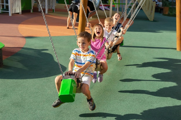 Children ride on a long swing on a modern playground sit behind each other and laugh