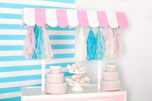 Children room with blue stripe. candy stall photo zone with big macaroons, sweets and marshmallows. trolley with ice cream.  Decorated room for a birthday. Cart with Candy Bar.