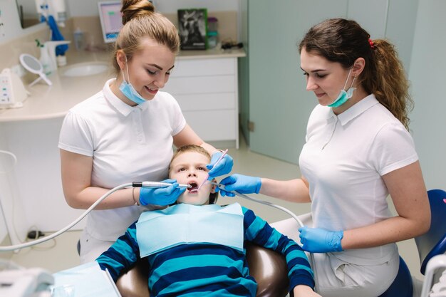 Children's dentist and assistant examination boy's teeth while he sitting on the dental chair at the office Female dentist