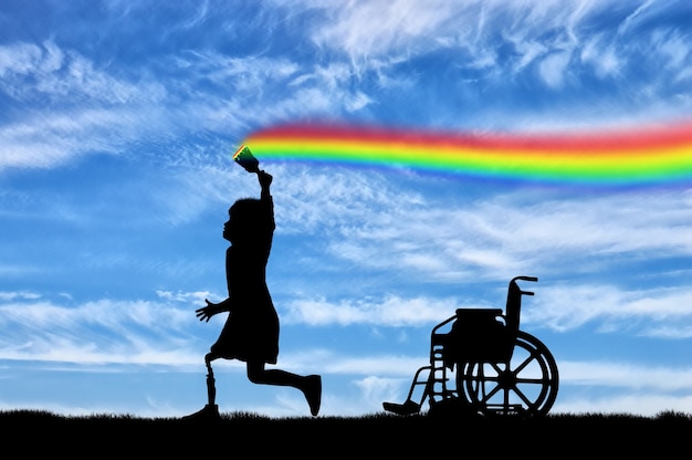 Children's disability concept. The child has a disability with a prosthetic leg with a brush in hand, runs, and draws a rainbow in the sky and next to wheelchair