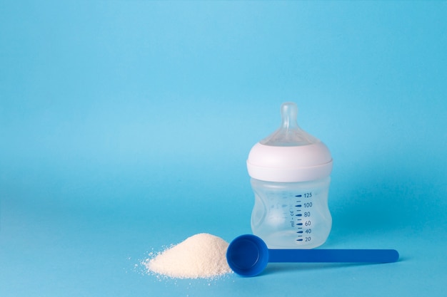 Children's dry mix for feeding, Measuring spoon, Feeding bottle with a pacifier on a blue background.