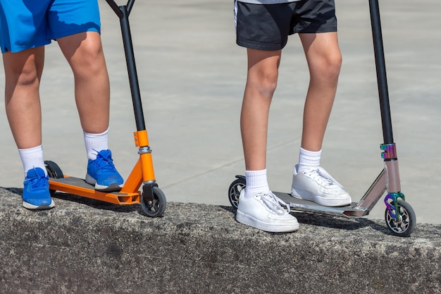 Children's feet on multi-colored scooters, two children, close-up, outdoor entertainment