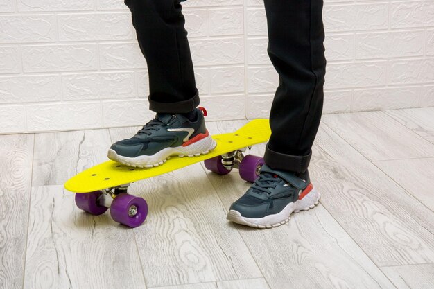 Children's feet in sneakers standing on a yellow skateboard