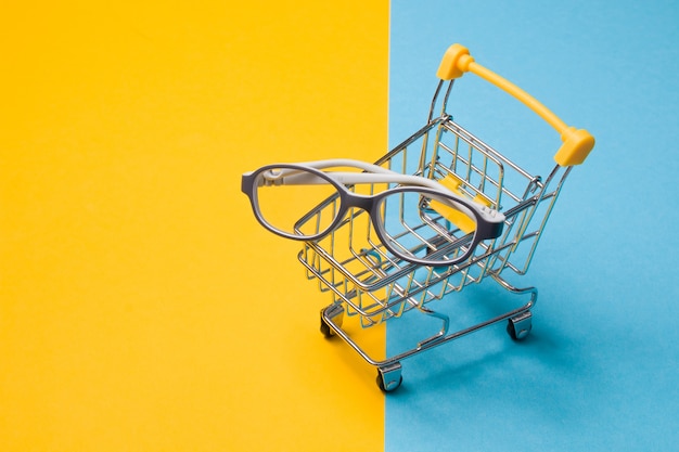 Children's glasses for small children in a gray plastic frame in a small shopping cart on a colorful surface