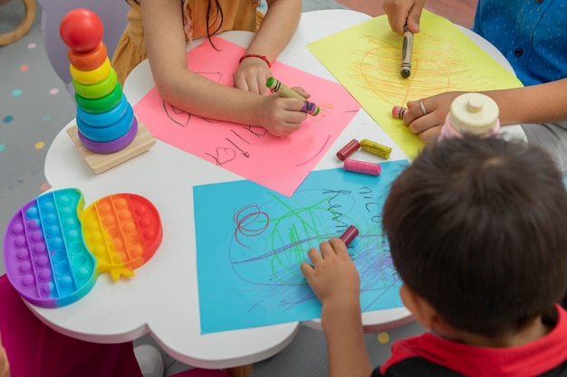 Children's hands drawing on colored sheets on a preschool table