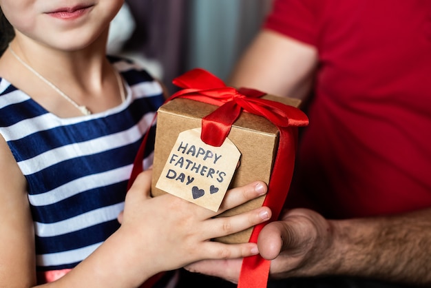 Children's hands give a box with a red bow and a postcard