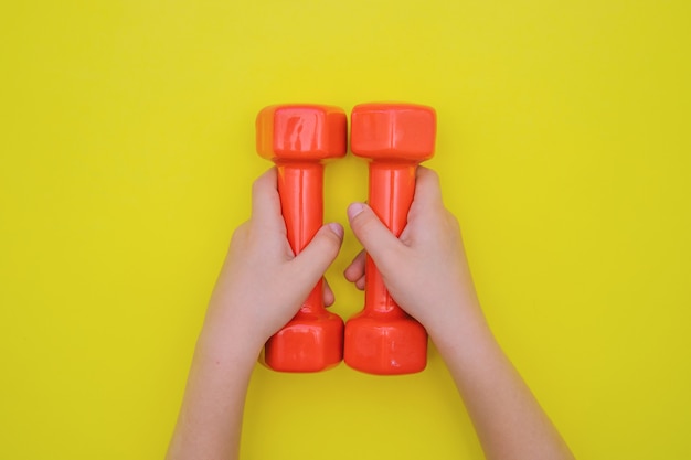 Children's hands hold red dumbbells. The concept of sports and a healthy lifestyle.