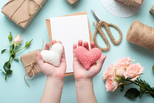 Children's hands hold two knitted hearts on the background of a vintage composition for Valentine's Day