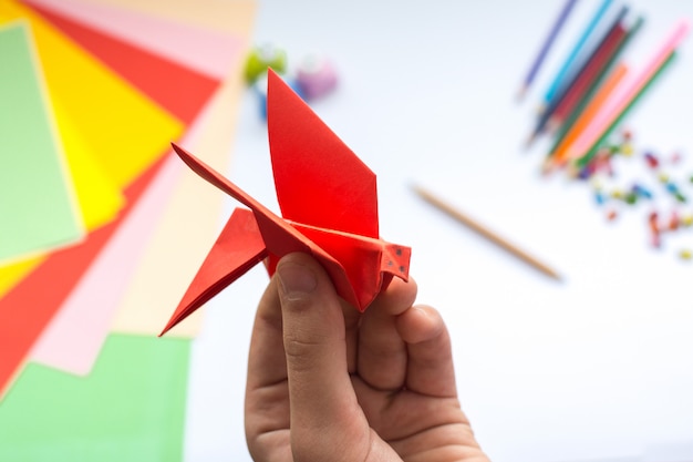 Children's hands do origami  bird from red paper